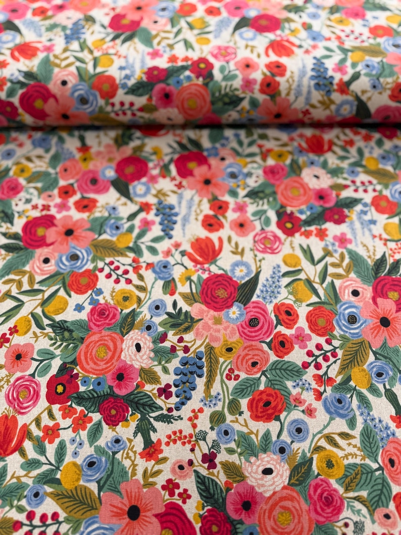 May include: A white fabric with a floral pattern featuring pink, red, blue, and green flowers. The fabric is folded in half, showing the pattern on both sides.