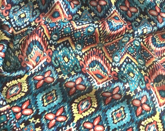 May include: A close-up of a fabric with a colorful geometric pattern. The pattern features shades of blue, red, yellow, and white. The fabric has a soft, flowing texture.