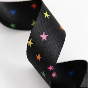 May include: Black ribbon featuring a repeating pattern of colourful stars in yellow, pink, orange, green, and blue. The ribbon is curled, displaying the pattern on both sides. Suitable for crafts or gift wrapping.