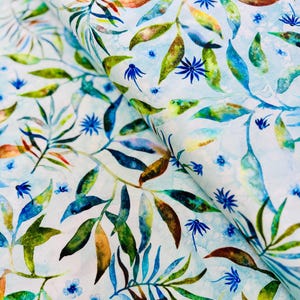 May include: Close-up of fabric with a watercolour design. It features green, blue, and brown leaves and small blue flowers on a light blue background. The fabric is folded, showing the repeating pattern.