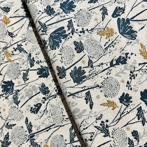 May include: A white fabric with a repeating pattern of blue and gold leaves and flowers. The fabric has a subtle texture.