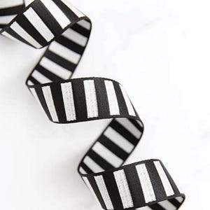 May include: A black and white striped ribbon, with a repeating pattern of vertical stripes. The ribbon is curled and twisted, creating a dynamic design. The ribbon is made of a woven fabric, suitable for crafts and decorations.