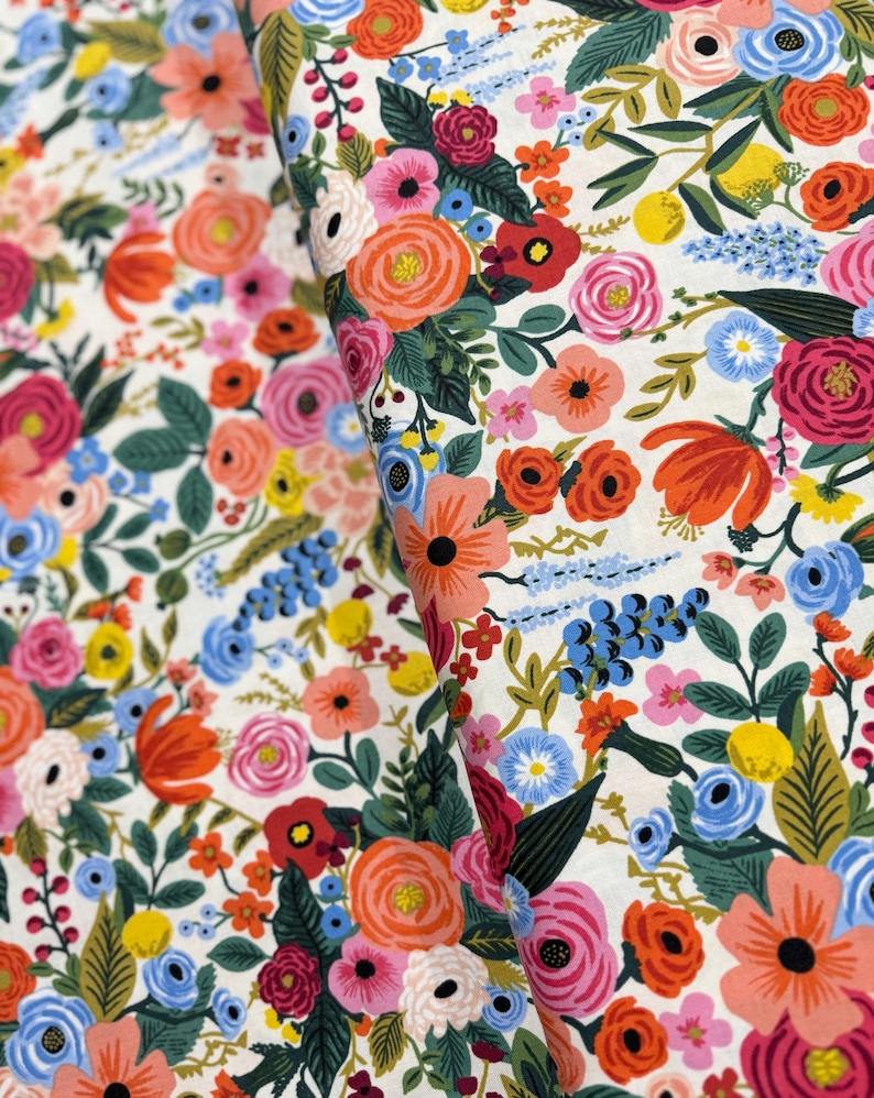 May include: A white fabric with a floral pattern featuring a variety of colorful flowers, including red, pink, orange, yellow, blue, and green. The flowers are arranged in a random pattern and are surrounded by green leaves.