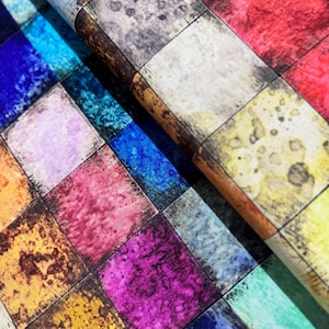 May include: A colourful fabric with a chequered pattern. Each square is a different colour, including red, blue, green, yellow, purple, and brown. The fabric has a textured, watercolour-like appearance.