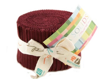 May include: A roll of burgundy fabric with a white ribbon tied around it. The fabric is labeled "Moda Solids".
