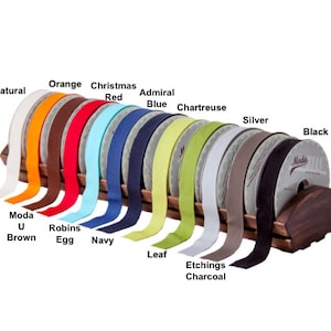 May include: A display of 14 spools of ribbon in various colours, including natural, orange, Christmas red, admiral blue, chartreuse, silver, black, brown, robin's egg, navy, leaf, and charcoal. The spools are arranged on a wooden stand.