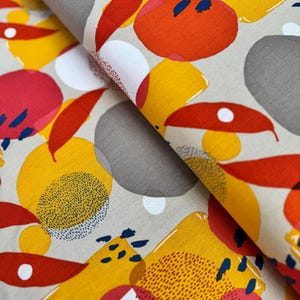 May include: Close-up of a fabric with a repeating pattern of abstract shapes in shades of red, orange, yellow, gray, and white on a beige background. The design includes dotted and solid elements, creating a vibrant and modern textile.