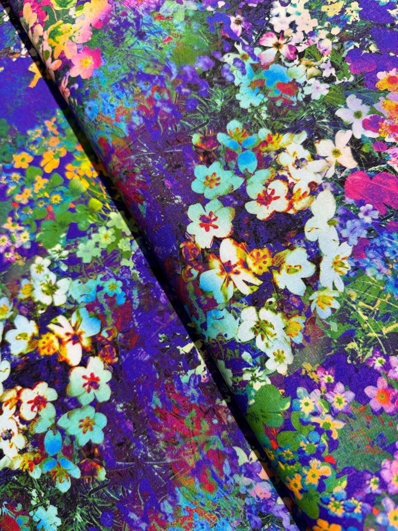 Op de afbeelding: Een paarse stof met een bloemenprint met witte, blauwe en gele bloemen. De stof heeft een textuur, bijna als een aquarel.