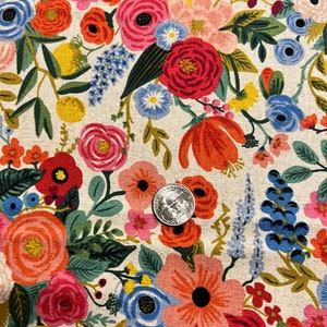 May include: A white fabric with a floral pattern featuring red, pink, blue, yellow, and green flowers. The fabric is covered in a variety of flowers, including roses, daisies, and other wildflowers.