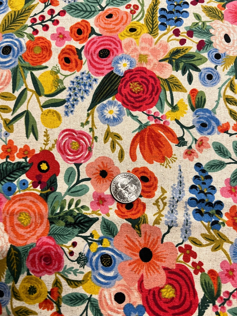 May include: A white fabric with a floral pattern featuring red, pink, blue, yellow, and green flowers. The fabric is covered in a variety of flowers, including roses, daisies, and other wildflowers.
