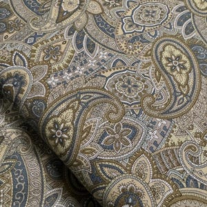 May include: A beige and blue paisley fabric with a repeating pattern of intricate designs. The fabric is soft and has a subtle sheen.