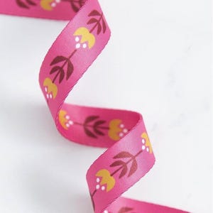 May include: A bright pink ribbon with a floral design. The pattern includes yellow tulip-shaped flowers, brown leaves, and white dots. The ribbon is curled, displaying the repeating pattern.
