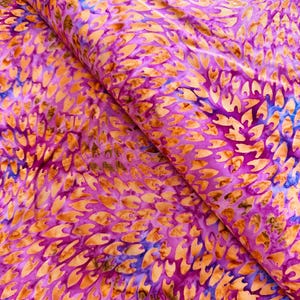 May include: A colourful fabric featuring a repeating pattern of leaf-like shapes in orange, purple, and blue. The fabric is folded, showing the texture and depth of the material. The design is reminiscent of batik.