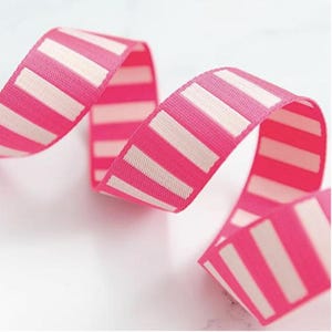 May include: A length of pink ribbon featuring a repeating pattern of white stripes. The ribbon is curled and appears to be made of a woven material. The bright colours and design suggest it could be used for gift wrapping or crafting.