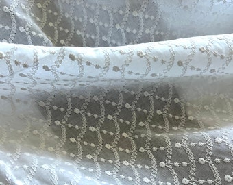 May include: White cotton fabric with a delicate embroidered pattern of small flowers and a geometric design. The fabric is sheer and has a soft, airy feel.