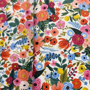 May include: A white fabric with a floral pattern featuring a variety of colorful flowers, including pink, red, orange, yellow, blue, and green.