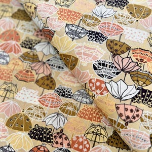 May include: A fabric with a repeating pattern of stylized umbrellas in various colors, including beige, pink, gold, and black. The umbrellas have decorative details and are arranged on a beige background. The fabric appears to be cotton or a similar material.