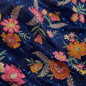 Könnte beinhalten: Nahaufnahme eines marineblauen Stoffes mit gestickten Blumenmustern in Rosa-, Orange- und Gelbtönen. Der Stoff ist mit Pailletten besetzt.