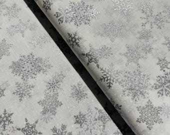 Può includere: Tessuto bianco con un motivo ripetitivo di fiocchi di neve argentati con glitter.
