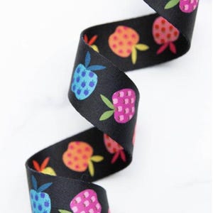May include: Black ribbon featuring a repeating pattern of colourful strawberries. The strawberries are in shades of blue, pink, and orange, with green leaves and yellow stems. The ribbon is curled and appears to be made of fabric.