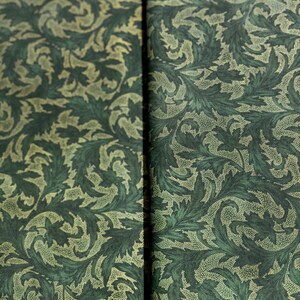 May include: A close-up of a green fabric with a repeating pattern of stylized leaves and dots. The leaves are a darker green and the dots are a lighter green.