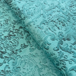 May include: Teal fabric with an embossed paisley pattern. The fabric has a soft, velvety texture.