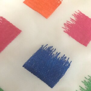 May include: A white fabric with a repeating pattern of colourful squares. The squares are filled with a textured brushstroke design in shades of orange, pink, blue, and green.