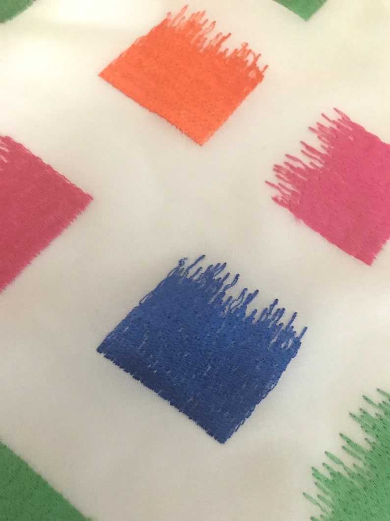 May include: A white fabric with a repeating pattern of colourful squares. The squares are filled with a textured brushstroke design in shades of orange, pink, blue, and green.