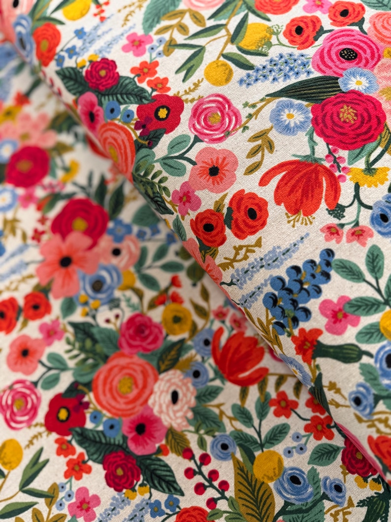 May include: A white fabric with a floral pattern featuring red, pink, blue, and yellow flowers. The fabric is folded in half, showing the pattern on both sides.