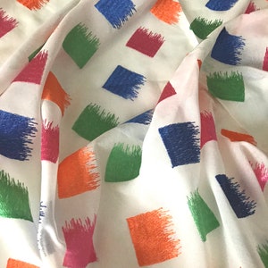 May include: White fabric with a repeating pattern of colourful squares. The squares are outlined in a brushstroke design and are in shades of blue, green, orange, pink, and red.