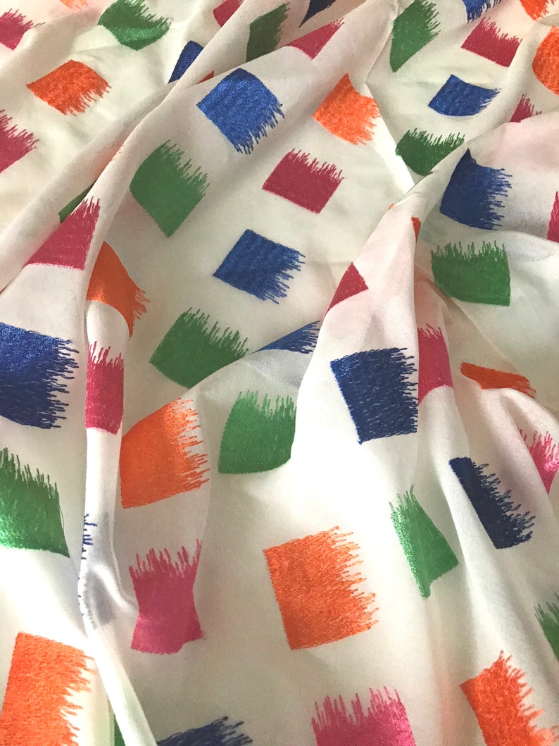May include: White fabric with a repeating pattern of colourful squares. The squares are outlined in a brushstroke design and are in shades of blue, green, orange, pink, and red.
