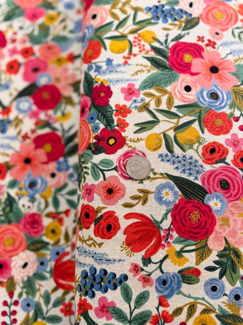 May include: A white fabric with a floral pattern featuring red, pink, blue, and yellow flowers. The fabric is covered in a variety of flowers and leaves.