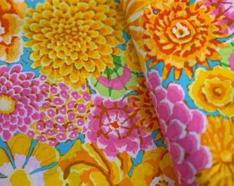 May include: A fabric featuring a vibrant floral pattern with large yellow, orange, and pink blossoms set against a bright turquoise background. The textile displays a dense arrangement of stylized flowers and leaves, with the word Enchanted printed on the edge.