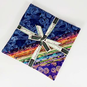 May include: A stack of 25 fat quarters of colorful batik fabric, tied together with a green and black ribbon. The fabric features a variety of patterns and colors, including blue, purple, orange, and green. The ribbon has the text "Island Batik" printed on it.