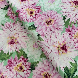 May include: A green fabric with a floral pattern featuring pink and white flowers with green leaves. The fabric has a delicate, vintage aesthetic.
