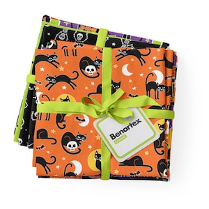 May include: A stack of four orange, black, and purple fabric squares with a black cat and skull design. The fabric is tied together with a green ribbon and a white tag that says "Benartex Canvas".