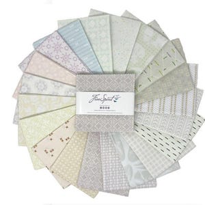 May include: A collection of fabric squares arranged in a circular pattern. The fabrics feature various patterns in shades of gray, cream, and pastel colors. A label with the text "Free Spirit" is visible in the center.