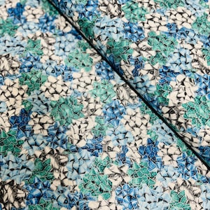 May include: A white fabric with a repeating pattern of blue and green bows. The bows are scattered randomly across the fabric.