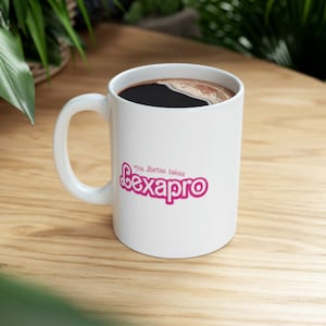 Può includere: Una tazza da caffè in ceramica bianca con un logo rosa che dice "The Sortie takes Lexapro" su una superficie di legno.