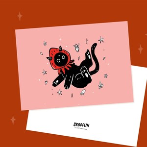 Pode incluir: Um gato preto vestindo uma fantasia de morango vermelho flutua no ar cercado por estrelas brancas e flores em um fundo rosa. O texto "SKOPFLIN ILLUSTRATIONS" est&aacute; em um fundo branco abaixo da imagem.