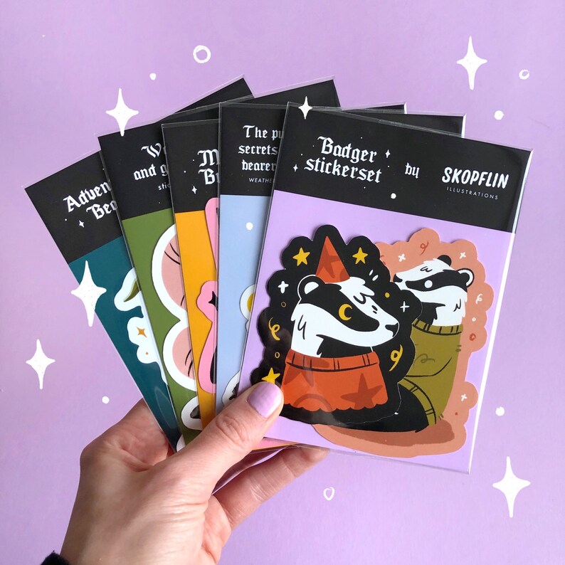May include: A set of six sticker sheets featuring illustrations of badgers, mushrooms, and other woodland creatures. The sticker sheets are black with white text and are packaged in a clear plastic sleeve. The text on the sticker sheets reads "Badger stickerset by Skoplin Illustrations".