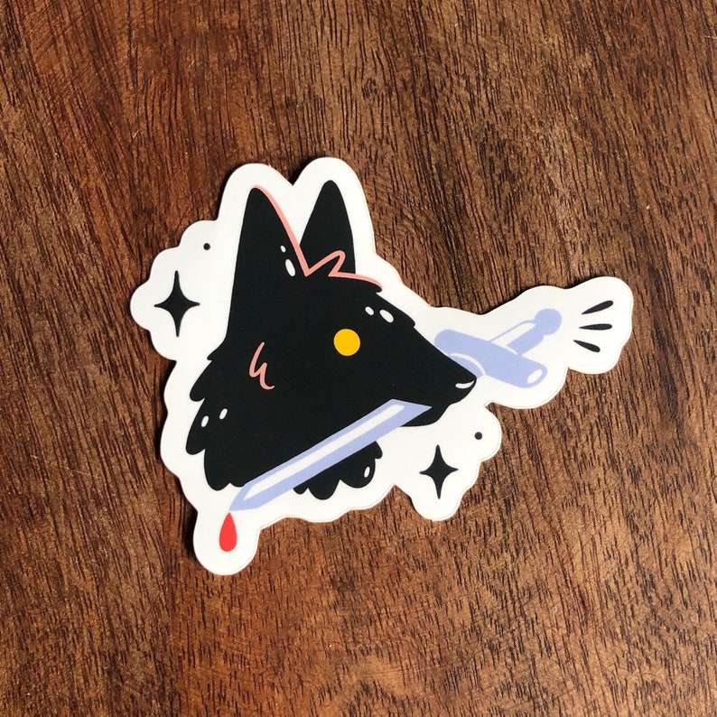 May include: A black wolf head sticker with a sword through it. The sword has a blue handle and a red drop of blood at the tip. The sticker has two white stars and a white starburst.
