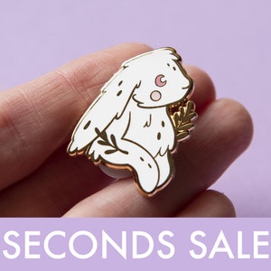 Può includere: Spilla in smalto dorata con un coniglio bianco con una luna crescente sulla fronte e un ramoscello di foglie. Il coniglio è contornato d'oro e ha un blush rosa sulla guancia.