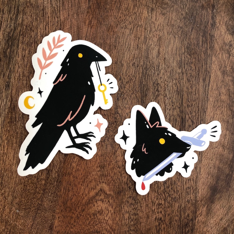 May include: Two black and white stickers featuring a crow with a key and a wolf's head with a sword through it.