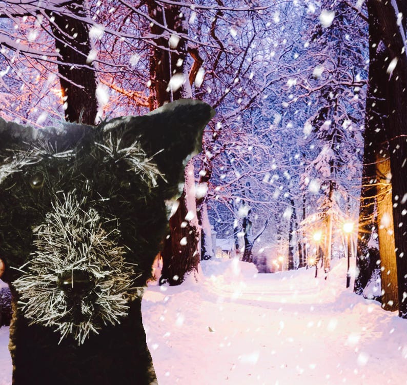 May include: A black dog's head is in the foreground, with a snowy winter forest scene in the background. The dog has a fluffy, textured appearance. The forest path is covered in snow, with falling snowflakes and streetlights.