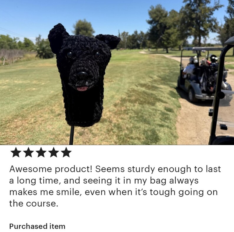 May include: Black crochet golf club head cover shaped like a dog's head. The cover has a detailed design with ears, a nose, and a tongue. The background shows a golf course with a golf cart.