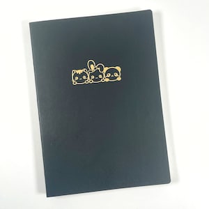 May include: A black notebook with a gold illustration of a cat, bunny, and bear. The notebook is closed and has a smooth, matte finish. The illustration is centered on the cover.