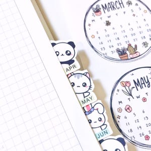 Peut inclure: Un agenda avec des onglets mensuels illustrés sur le thème des animaux pour avril, mai et juin. Les onglets présentent un panda, un chat et un lapin. L'agenda comprend également un calendrier de mars avec des illustrations florales et végétales.