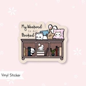 Peut inclure: Un autocollant en vinyle représentant une étagère avec le texte "My Weekend Is All Booked". L'autocollant comprend des illustrations d'un chat, d'un panda, d'un lapin, de livres, d'oreillers et d'un cactus. Fond rose clair.