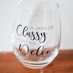 Puede incluir: Una copa de vino de vidrio transparente con el texto "A little bit Classy A little bit Delco" impreso en el lateral.